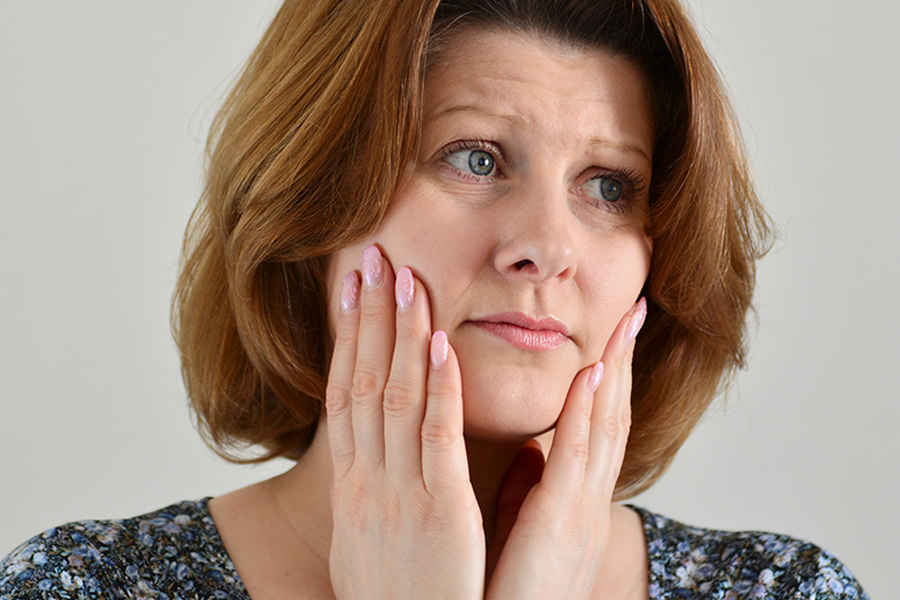 grinding teeth-new Sad woman experiencing jaw pain from grinding her teeth